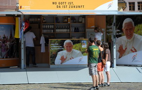 People look at the shopfront selling candles, mugs and flask near a poster  of Pope's Benedict XVI in a shop on September 2, 2011 on the cathedral square in Freiburg, southwest Germany.   Benedict XVI will visit  Germany from 22 to 25 September.            AFP PHOTO/FREDERICK FLORIN