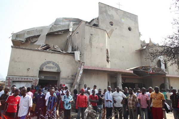 People stand in front of the partially destroyed St Theresa Catholic Church after a bomb blast in the Madala Zuba district of Nigeria's capital Abuja on December 25, 2011. Two explosions near churches during Christmas Day services in Nigeria, including one outside the country's capital, killed at least 28 people amid spiralling violence blamed on an Islamist group. The suspected attacks stoked fear and anger in Africa's most populous nation, which has been hit by scores of bombings and shootings attributed to Islamist group Boko Haram, with authorities seemingly unable to stop them. AFP PHOTO / Sunday Aghaeze