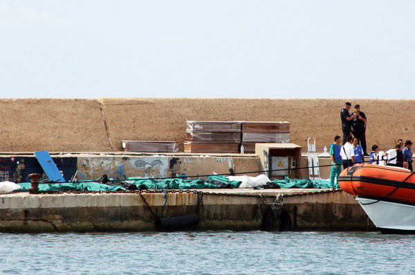 TOPSHOTSItalian policemen and rescue workers stand next to the covered bodies of migrants at Lampedusa port on October 3, 2013. At least 82 asylum-seekers drowned and 150 were rescued after a boat carrying some 500 people caught fire and capsized near an Italian island, officials and media reports said. AFP PHOTO/STR
