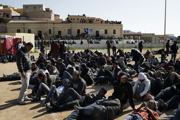 Tunisian immigrants wait on a soccer field to be transfered to a temporary facility after their arrival on the Italian island of Lampedusa on February 13, 2011. Italy said the same day it was planning to deploy its security forces in Tunisia to stop a wave of immigrant arrivals, as coastguards intercepted another 1,000 immigrants from the North African state. AFP PHOTO / ROBERTO SALOMONE