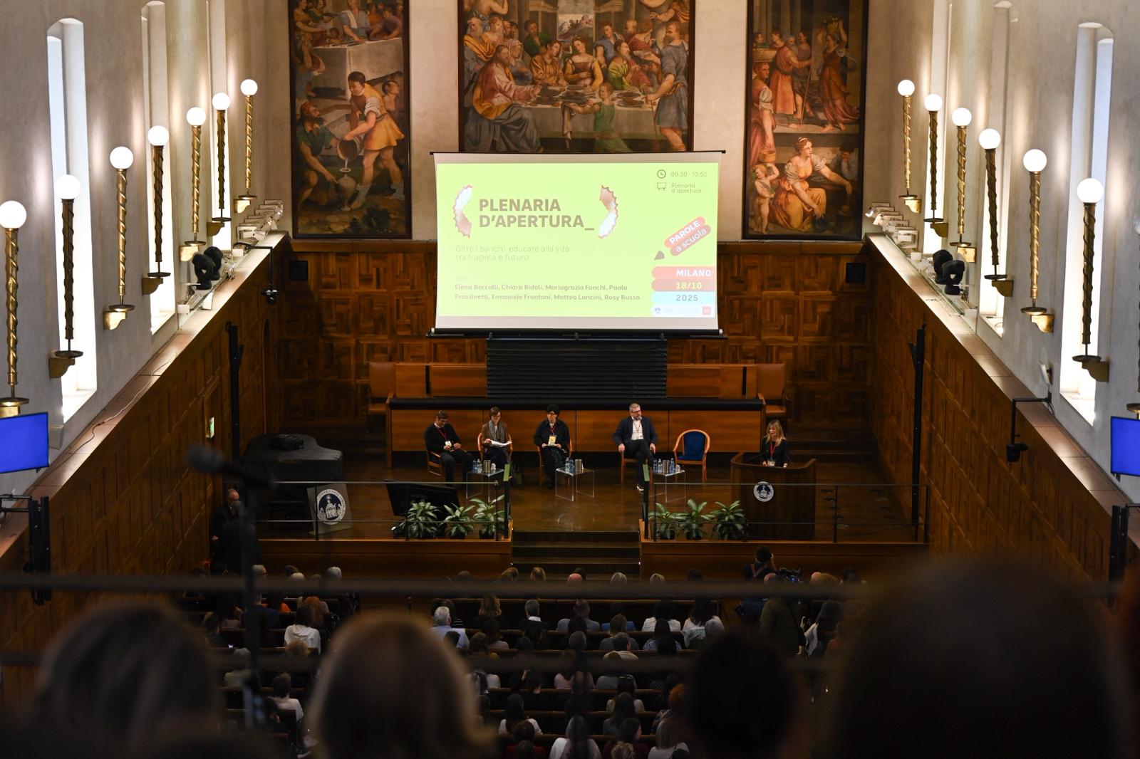 Veduta della sala conferenze con relatori sul palco e pubblico seduto, durante la plenaria d’apertura di un evento.