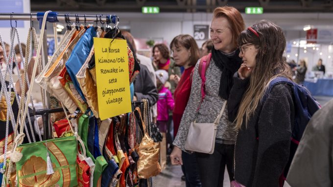 Visitatori osservano borse colorate realizzate con kimono giapponesi vintage esposte su uno stand della fiera Fa’ la cosa giusta!, con un cartello informativo appeso al supporto.
