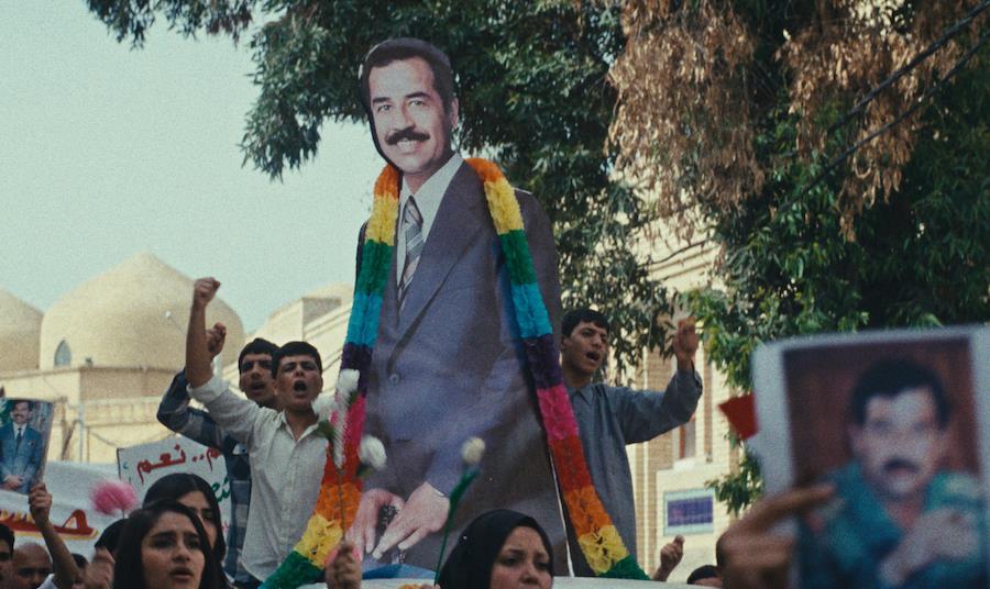 Una folla con un grande ritratto di Saddam Hussein durante una manifestazione in una scena del film ‘La torta del Presidente’